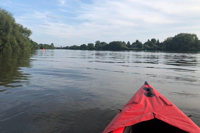 Un río tranquilo con un kayak rojo en primer plano y árboles a lo largo de las orillas. 4