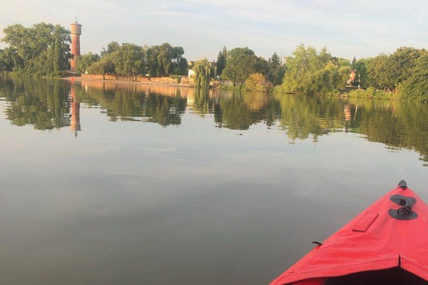 Un lago tranquilo con un kayak rojo, árboles y una torre al fondo. 2
