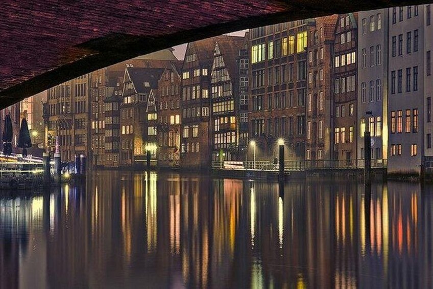 Une vue nocturne d’une rivière, avec les bâtiments qui se reflètent dans l’eau, un pont et des lampadaires. 2