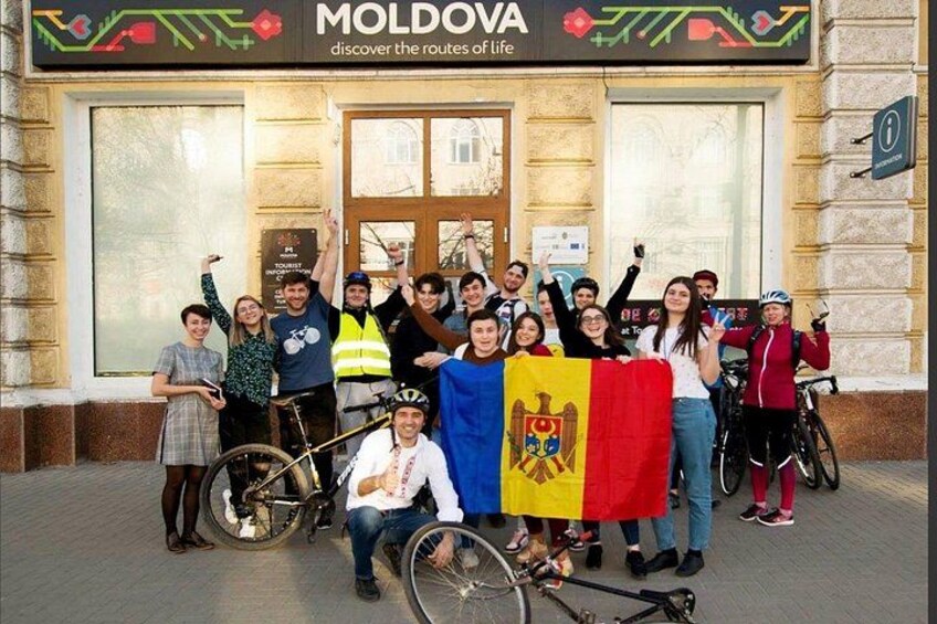 A group of people in front of a building with a sign that reads 'MOLDOVA discover the routes of life'. 1