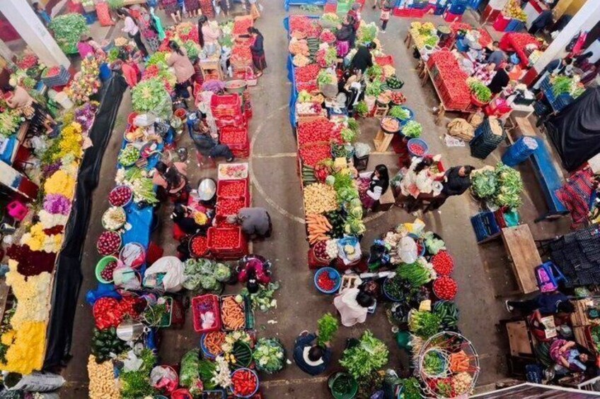 An aerial view of a bustling outdoor market with various stalls selling fruits, vegetables, and flowers. 2