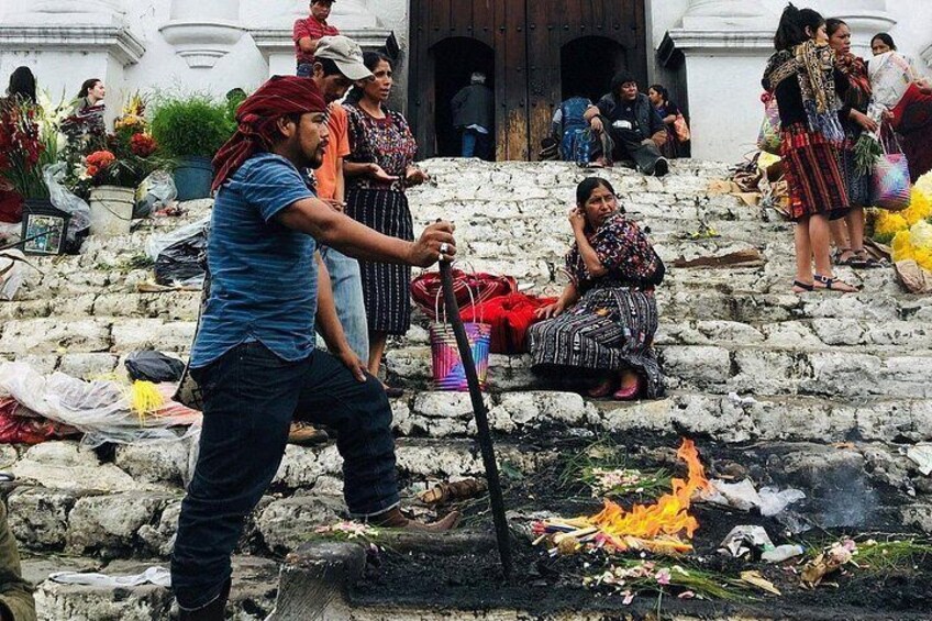 A person performing a ritual with a fire on stone steps, surrounded by people in traditional attire. 4