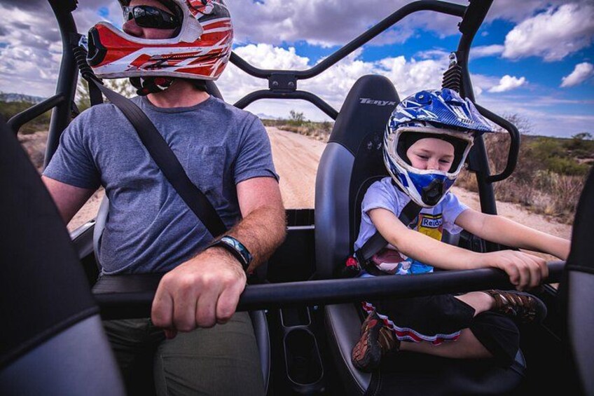 A man and a child in a vehicle with a helmet, driving on a dirt road. 4