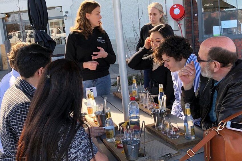 Een groep mensen verzameld rond een tafel met flessen en glazen, mogelijk op een evenement of bijeenkomst buiten. 2