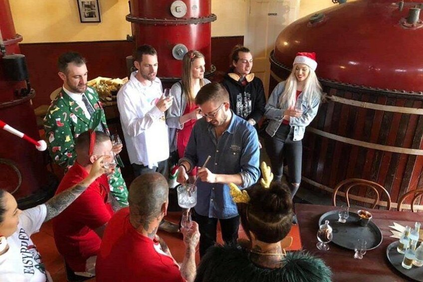 Een groep mensen in een feestelijke binnensfeer, met een groot, rood, cilindervormig object op de achtergrond. 1