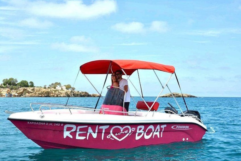 A red and white boat with a red canopy, labeled 'RENT A BOAT,' on calm water with a rocky coastline in the background. 1