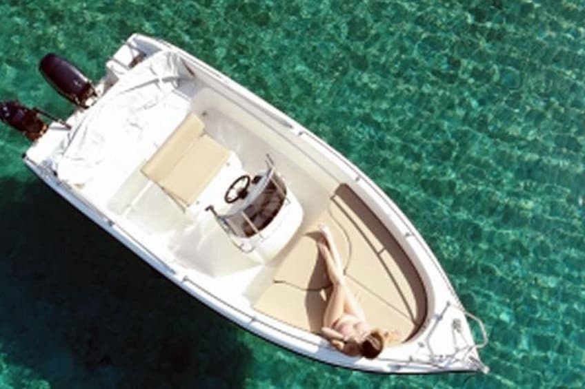 A small white boat with a person lying on the deck, floating on clear blue water. 4