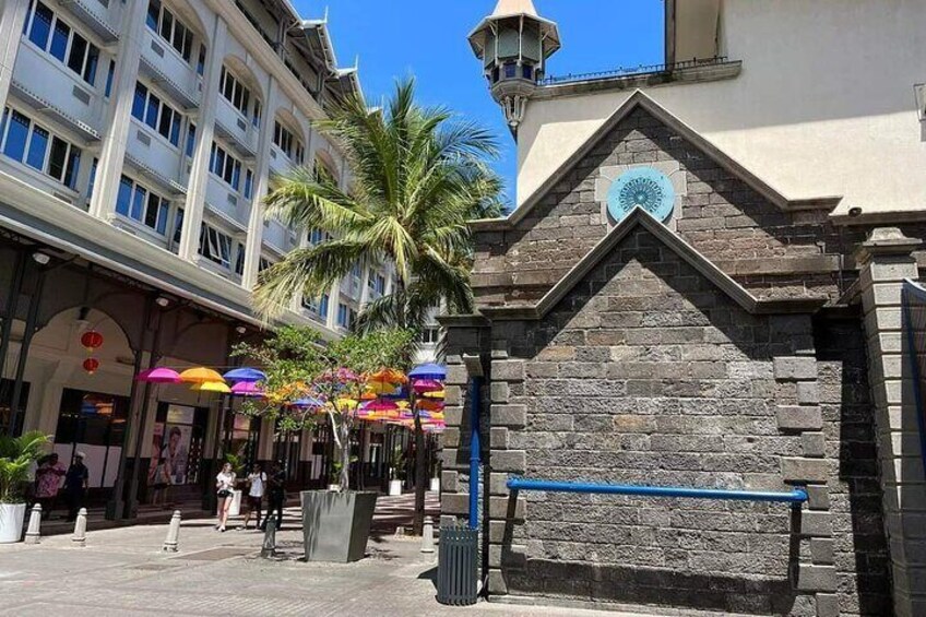 A street with a stone building, palm trees, and colorful umbrellas. 4