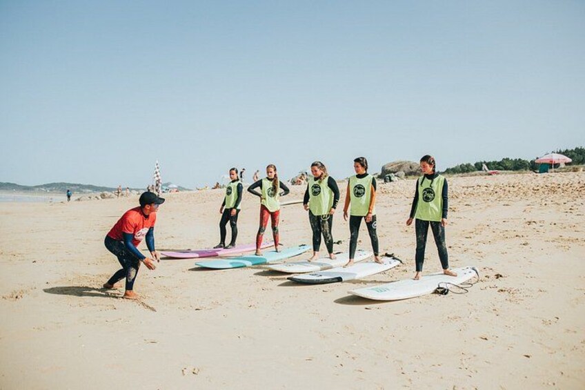 A group of people on a beach with surfboards, some wearing wetsuits and life vests. 3