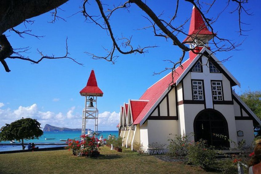 A church with a red roof and a bell tower, surrounded by a grassy area and a body of water. 5