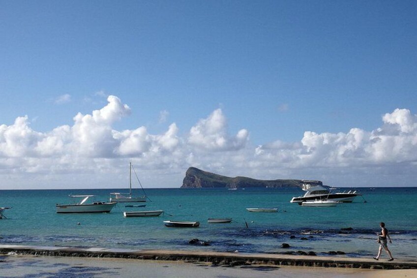 A beach with boats, a person walking, and a large rock formation in the distance. 3