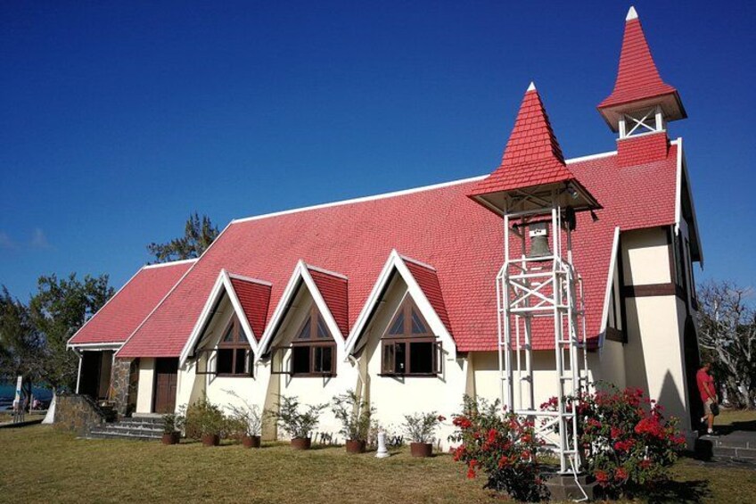 A church with a red roof and white walls, a bell tower, and a small garden with red flowers. 4