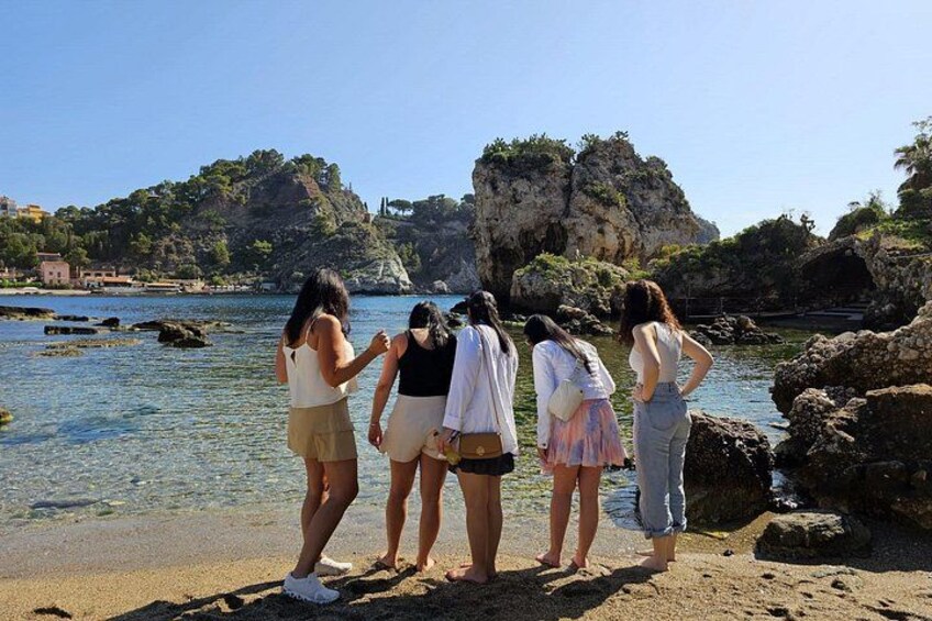 Un groupe de personnes se tient sur une plage, avec une eau claire et des falaises rocheuses en arrière-plan. 5
