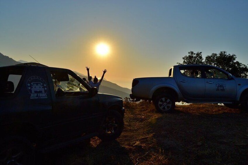 Two pickup trucks parked on a dirt road with the sun setting in the background. 4