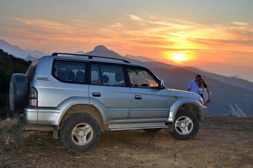 A silver SUV parked on a dirt road with a sunset in the background. 3