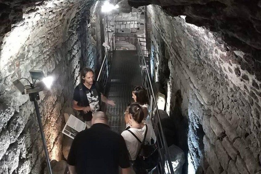 A group of people in a narrow, rocky tunnel with metal railings and artificial lighting. 1
