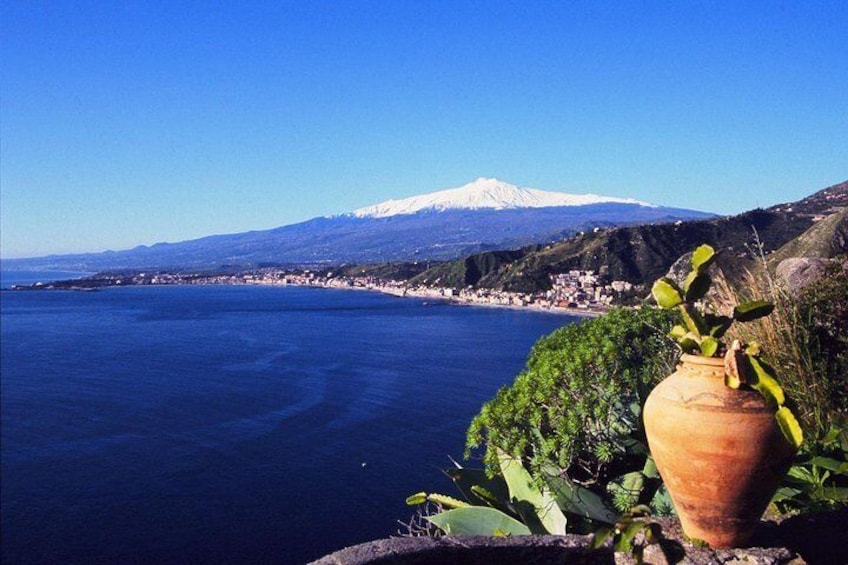 A coastal landscape with a mountain in the background, a body of water, and a terracotta pot with plants. 5