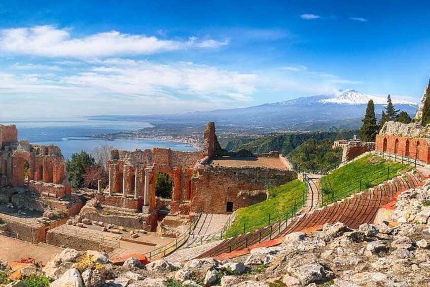 Ancient ruins with columns, a theater, and a mountainous landscape in the background. 1