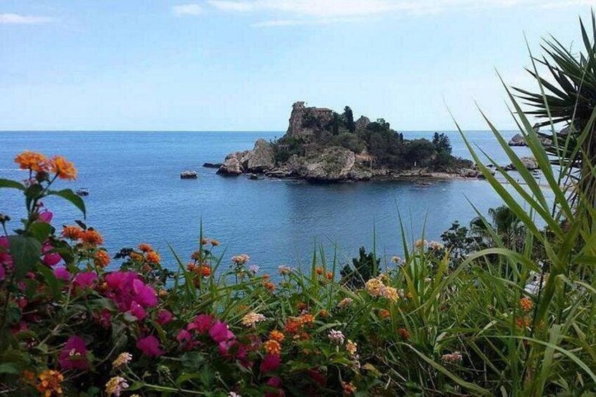 A coastal landscape with a rocky outcrop, a clear blue sea, and vibrant flowers in the foreground. 4