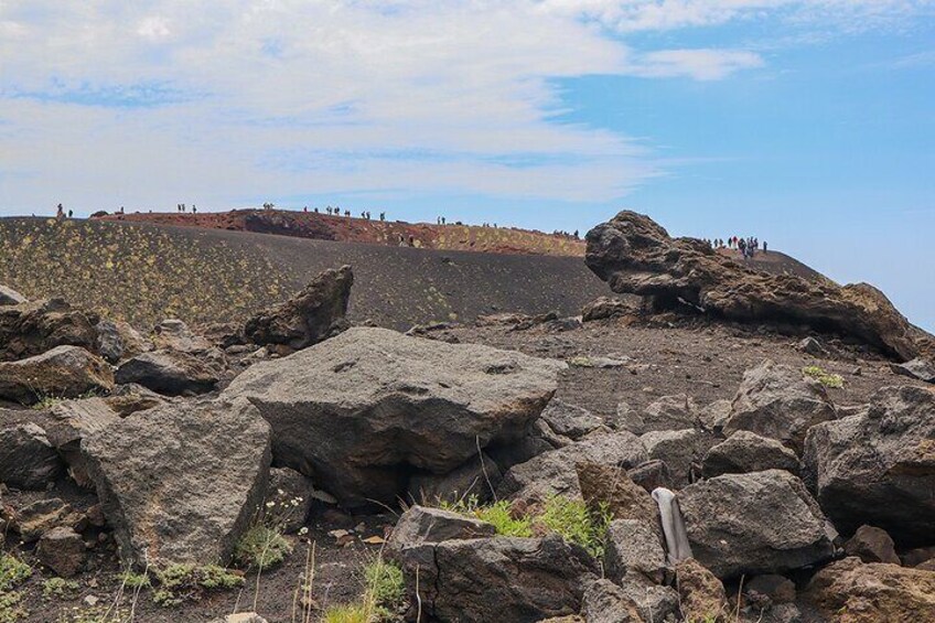 A rocky landscape with large boulders and a group of people on a hill in the background. 4