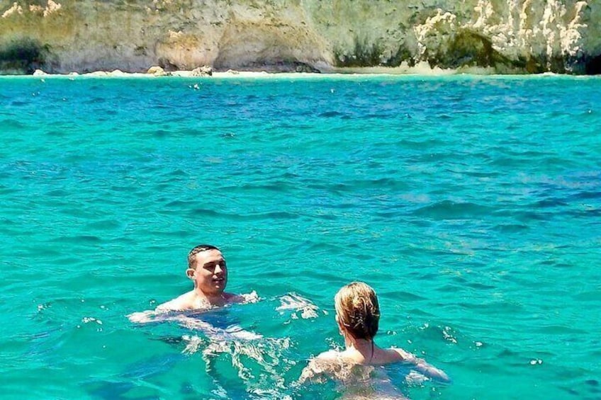 Zwei Personen schwimmen in klarem türkisblauem Wasser, im Hintergrund eine felsige Küste. 3