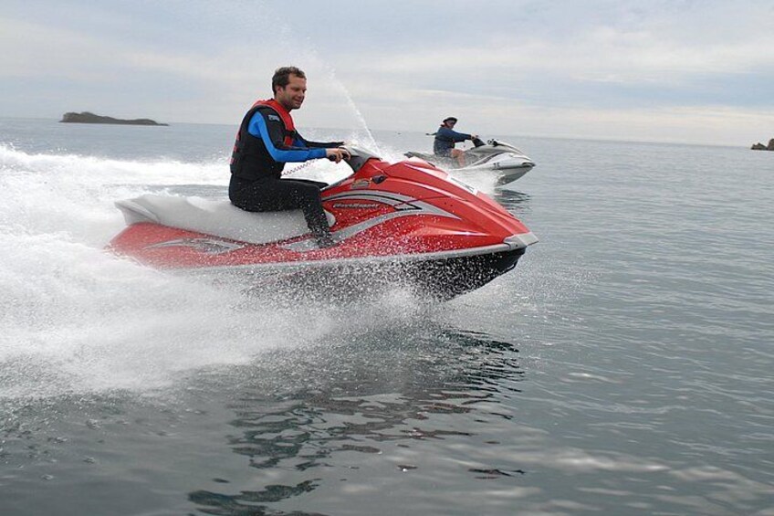 A person riding a red jet ski on calm water with another jet ski in the background. 2