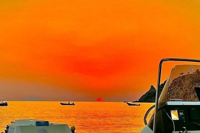 A sunset over a body of water with boats and a rocky island in the distance. 3