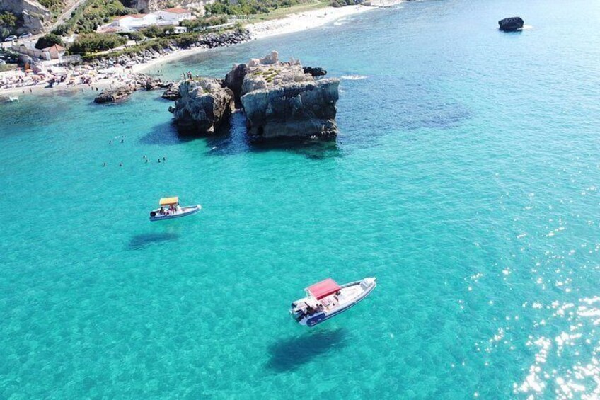 A coastal area with clear turquoise water, rocky outcrops, and boats. 2