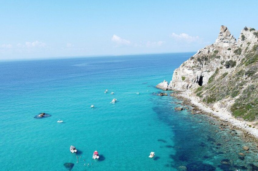 A coastal landscape with clear turquoise waters, boats, and rocky cliffs. 2