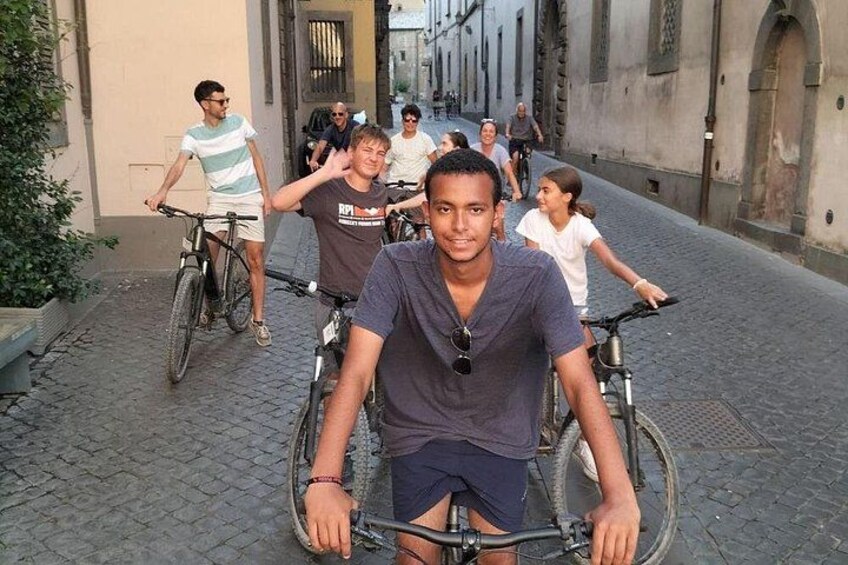 A group of people on bicycles in a narrow street with historic buildings. 2