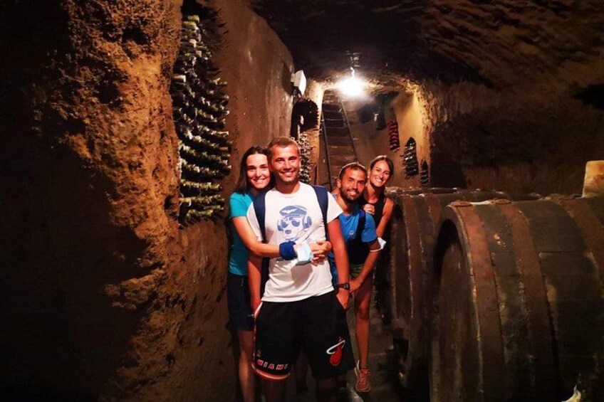 A group of people in a dimly lit cave with rough walls and a large wooden barrel. 3