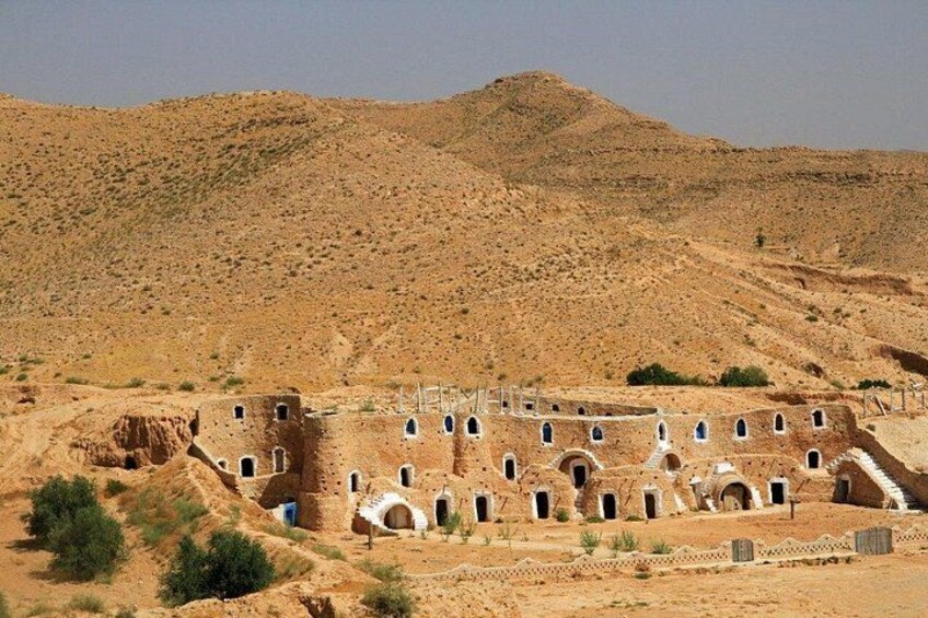 A desert landscape with ancient ruins featuring multiple arches and a large central structure. 2
