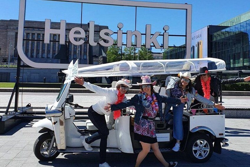 A white electric vehicle parked in front of a building with the sign 'Helsinki'. 1