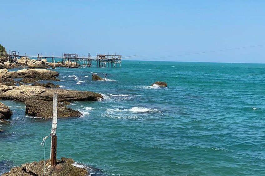 Eine felsige Küstenlinie mit einem Holzpfahl, klares blaues Meer und ein Steg, der sich ins Wasser erstreckt. 2