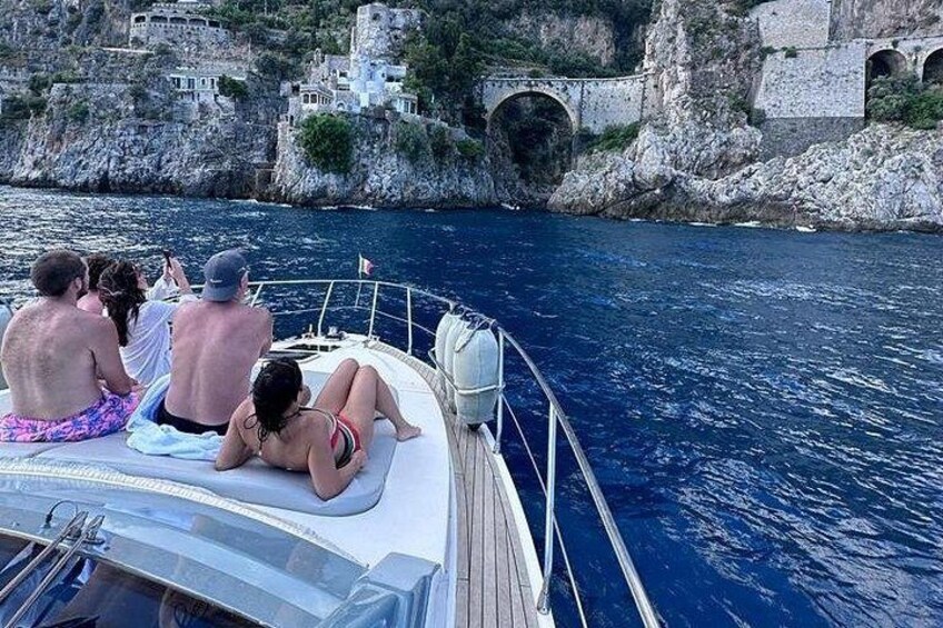 Un bote con gente en la cubierta, una costa rocosa y un puente de piedra. 5