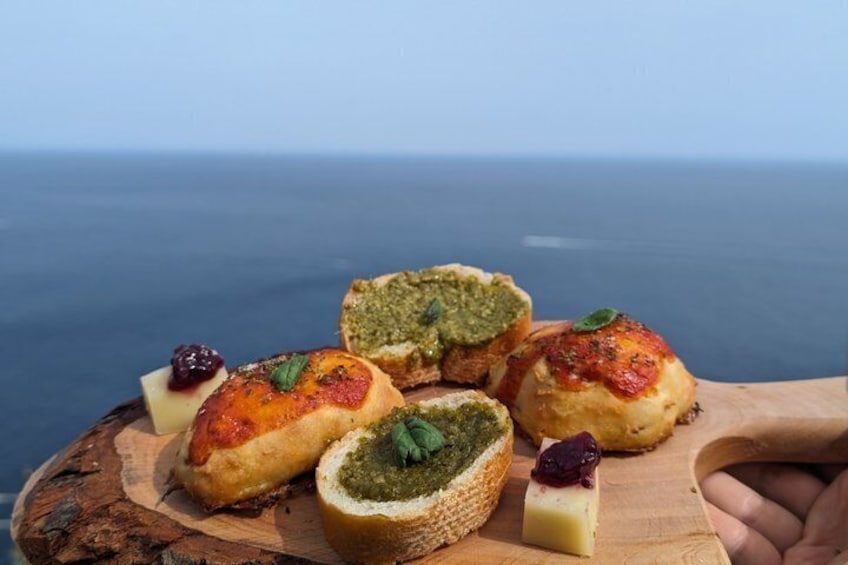 A wooden board with pastries and cheese, with a view of the sea in the background. 4