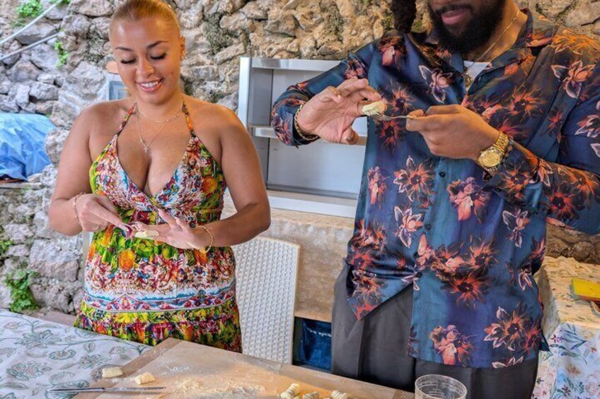 Two people preparing food, with a stone wall and a kitchen counter in the background. 5