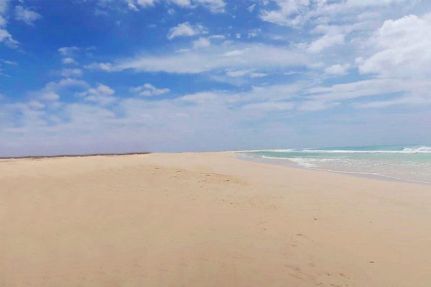 A wide sandy beach with gentle waves approaching the shore under a partly cloudy sky. 5