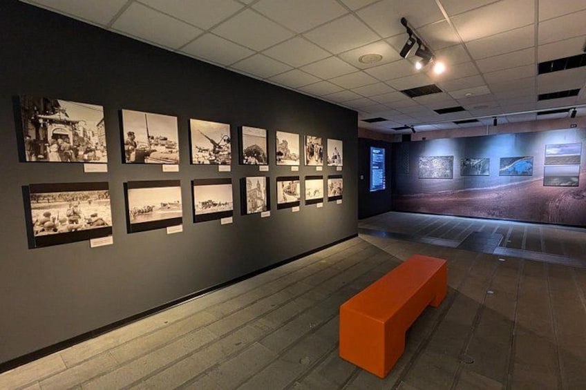 Una exhibición interior con fotografías en blanco y negro en las paredes, piso de madera y un banco naranja. 3