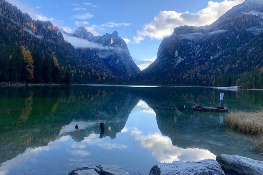 Un lago tranquilo rodeado de montañas, con aguas claras que reflejan el cielo y los árboles, y un pequeño muelle. 2