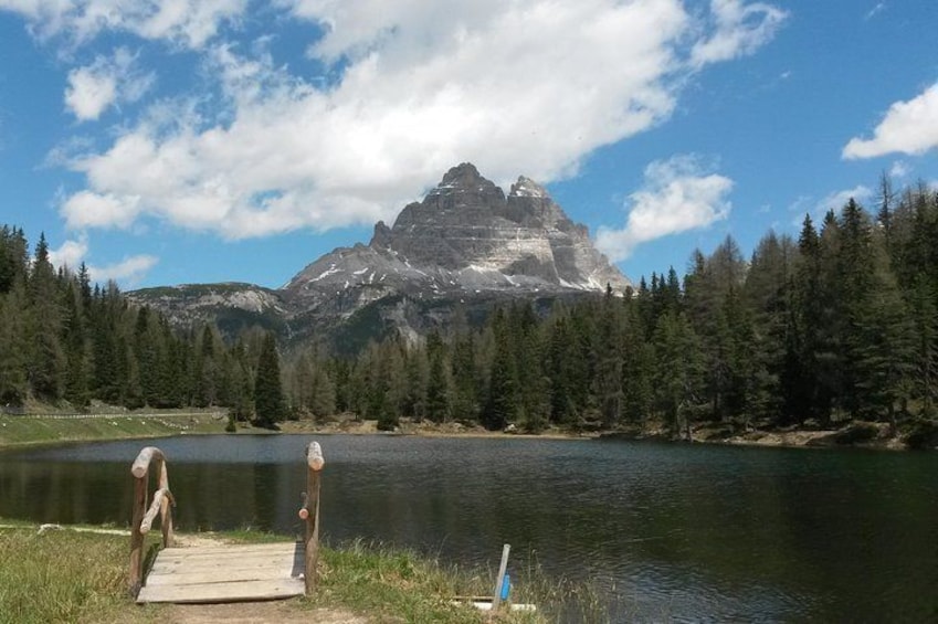 Un lago con un muelle de madera, rodeado de un bosque denso y una montaña imponente al fondo. 1