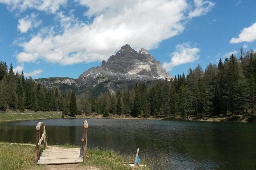 Un lago con un muelle de madera, rodeado de un bosque frondoso y una montaña imponente al fondo. 1