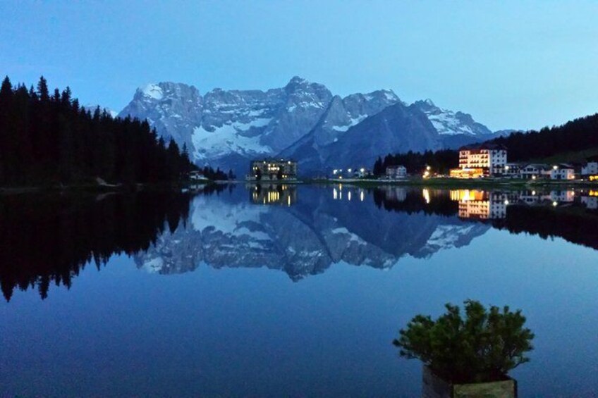 Un lago tranquilo que refleja montañas y edificios al atardecer. 4