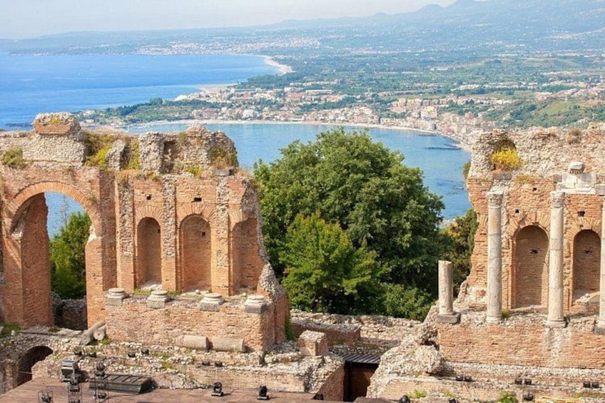 Ancient ruins with arches, a tree, and a coastal cityscape in the background. 1