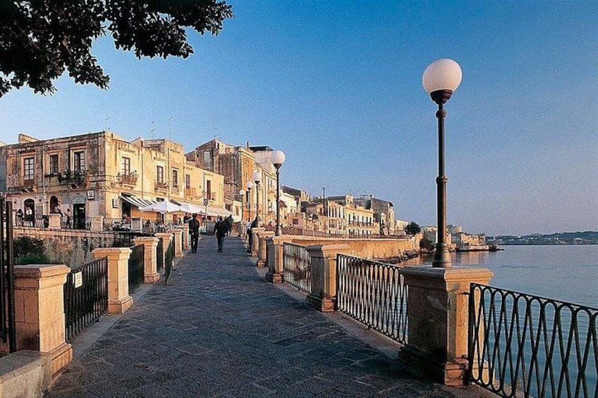 Un sendero de piedra que conduce a un muelle con edificios a un lado y una barandilla al otro. 3