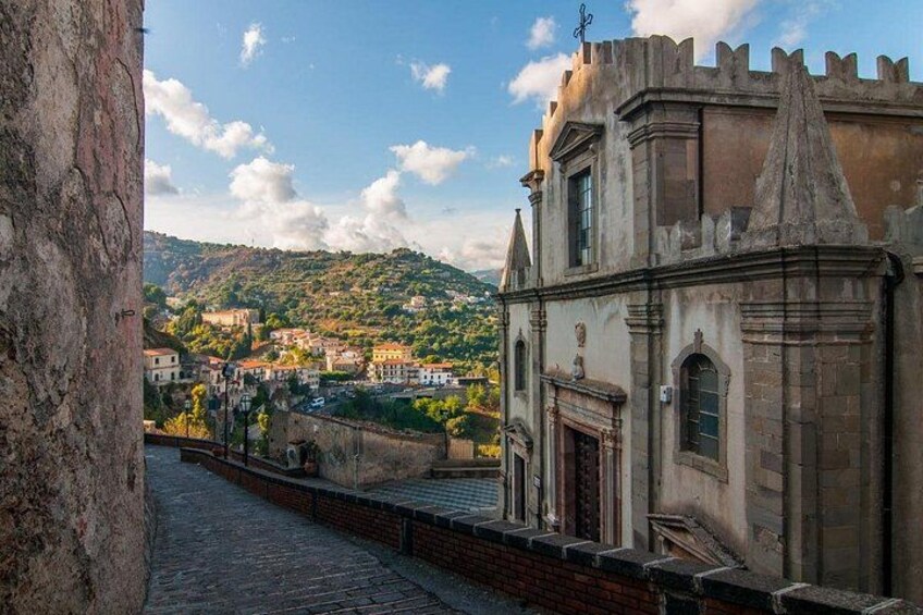 Una calle adoquinada, un edificio histórico con una torre y un paisaje urbano con colinas al fondo. 3