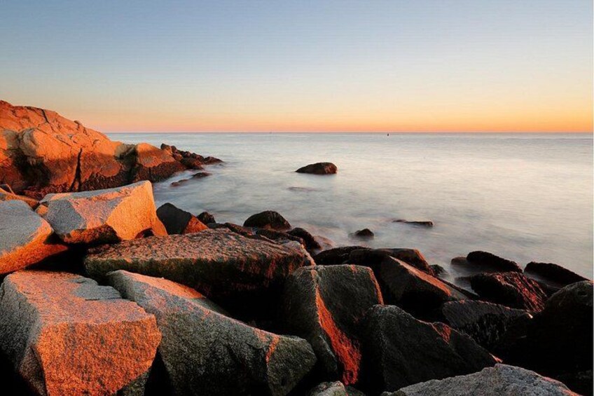 Een rotsachtige kustlijn met grote rotsblokken en rustig water bij zonsondergang. 3