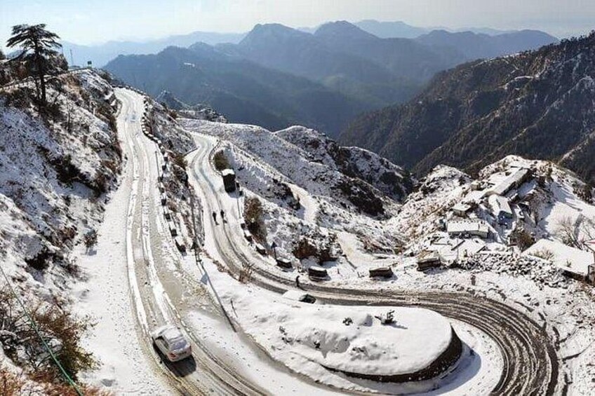 A winding mountain road with snow-covered terrain and a vehicle navigating the curves. 3