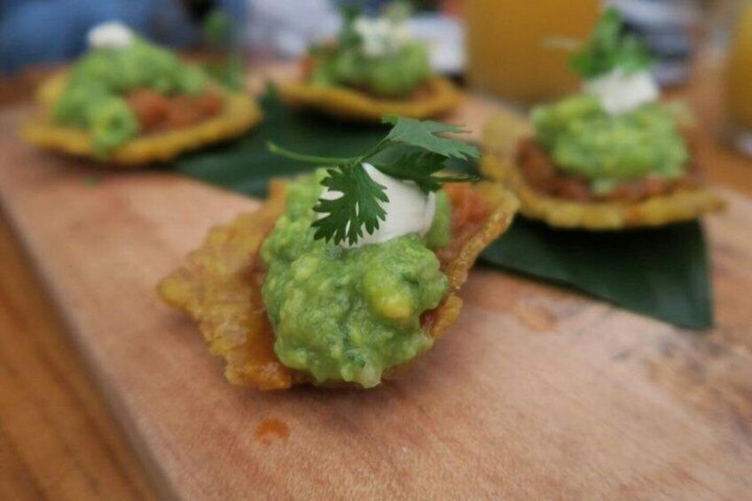 A food item with a green topping, possibly guacamole, on a crispy base, garnished with a leaf and a dollop of cream. 4