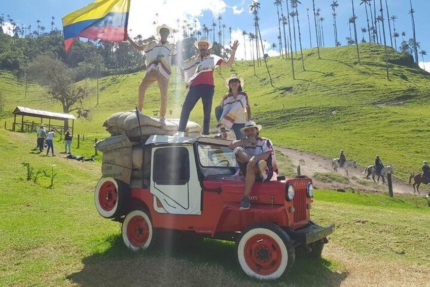 A red vehicle with people standing on top, surrounded by a grassy area with palm trees and a clear sky. 1